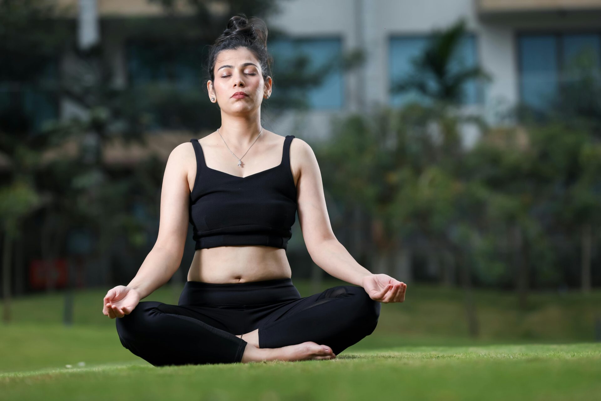 Eine junge Frau meditiert in einem Park und praktiziert Yoga in einer ruhigen Umgebung im Freien.