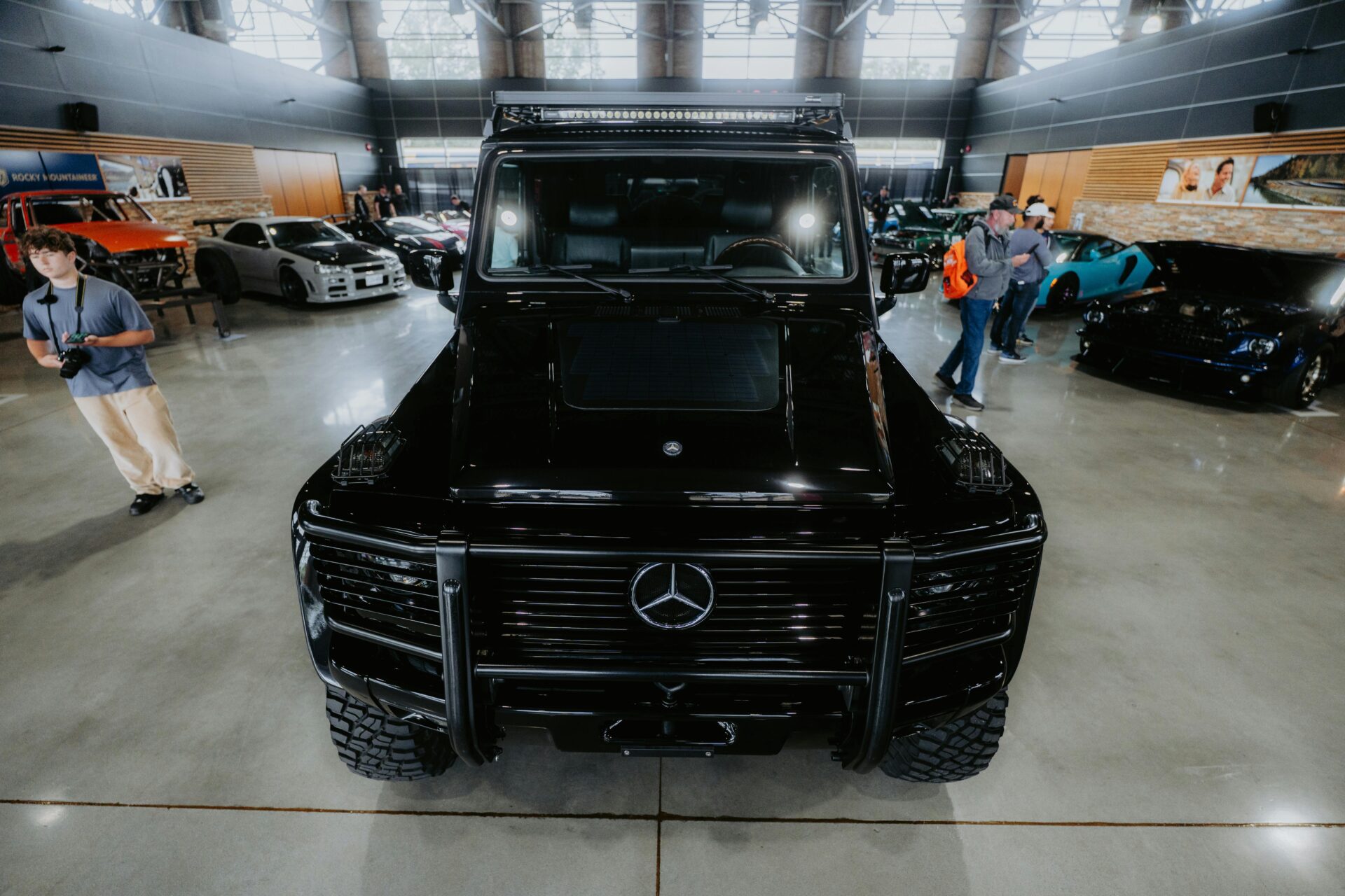 Vorderansicht eines schwarzen Luxus-SUV, der zusammen mit anderen Fahrzeugen auf einer Indoor-Automesse ausgestellt ist.