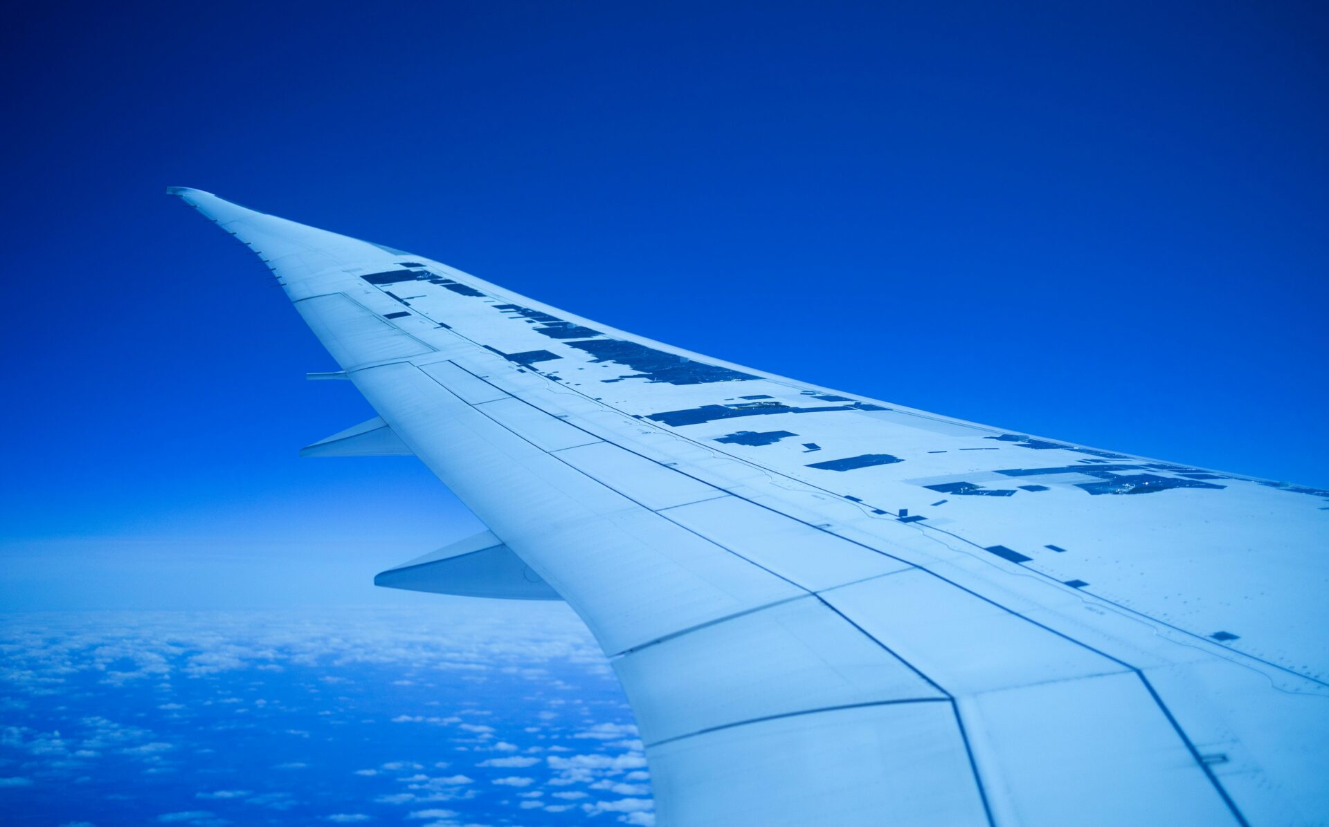 Blick auf einen Flugzeugflügel, der hoch über den Wolken vor dem Hintergrund eines klaren blauen Himmels fliegt.