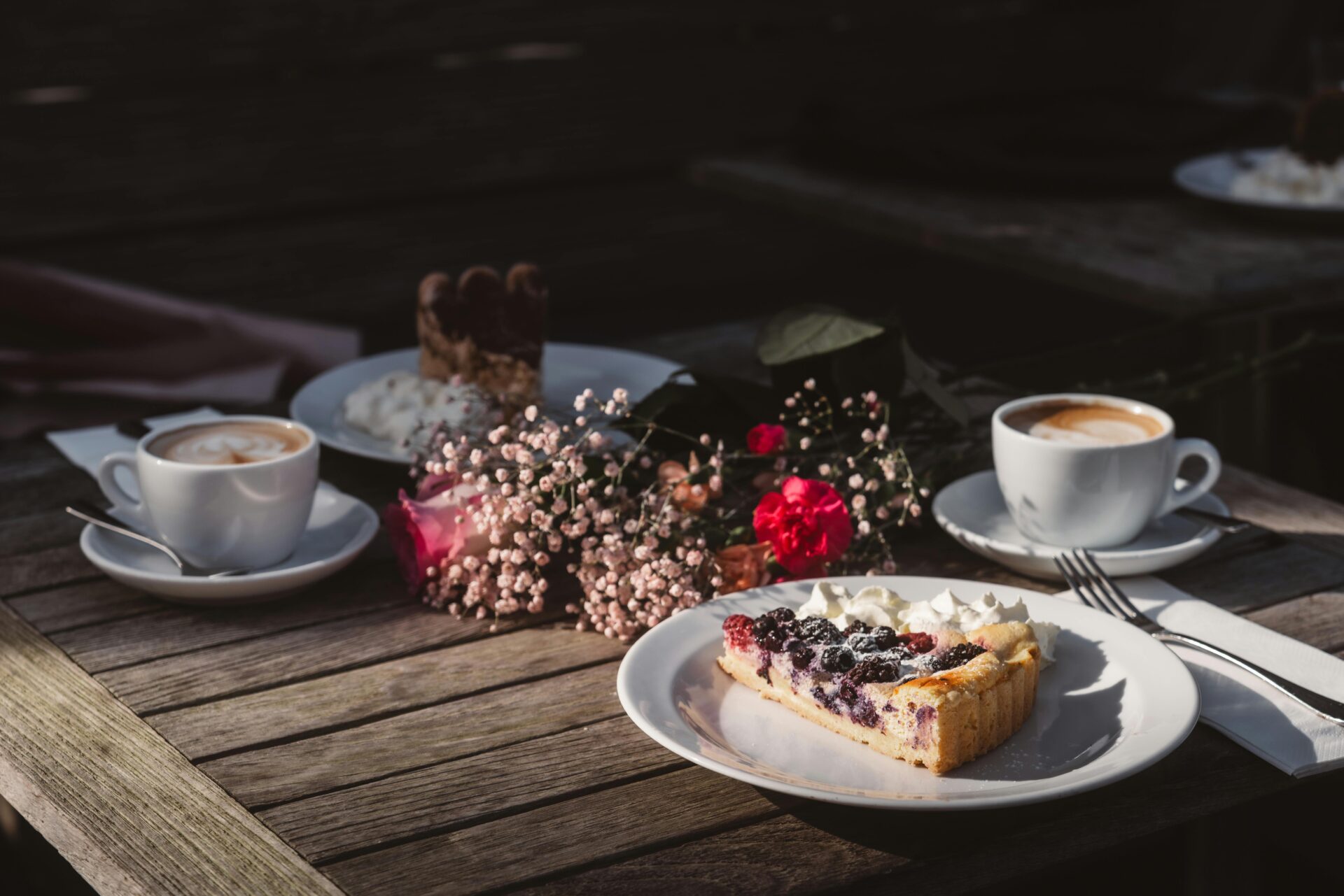 Eine warme, einladende Atmosphäre im Freien mit Kaffee, Beerentarte und Blumen – perfekt für einen entspannten Nachmittag.